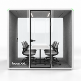 FocusPod Max front studio view with optional six-chair meeting furniture package and white logo low on the left glass.