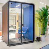 FocusPod Solo Plus in an office setting with blue ergonomic chair and interior panels, and FocusPod sticker low on the left glass.